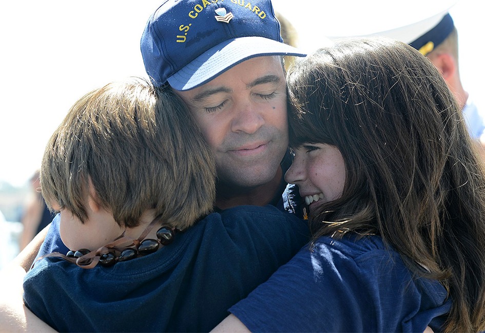 Coast Guard father in uniform hugging two young children