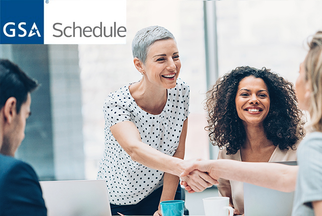 group of employees smiling, two business women shaking hands in office