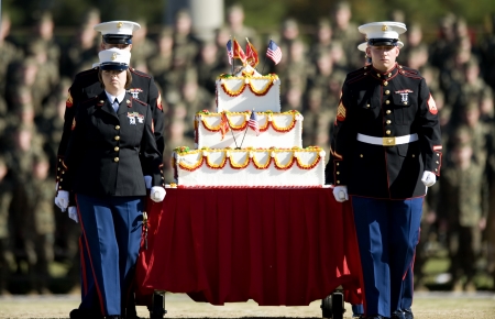 Marines in uniform carrying large cake with flags on table.