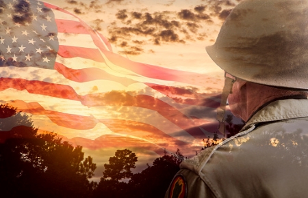 Solider looking off into sunset with American Flag faded into the sky.